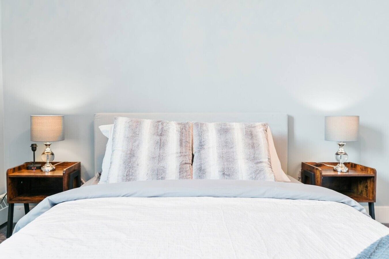 Un lit avec un oreiller à rayures, deux tables de chevet avec des lampes et un mur uni.