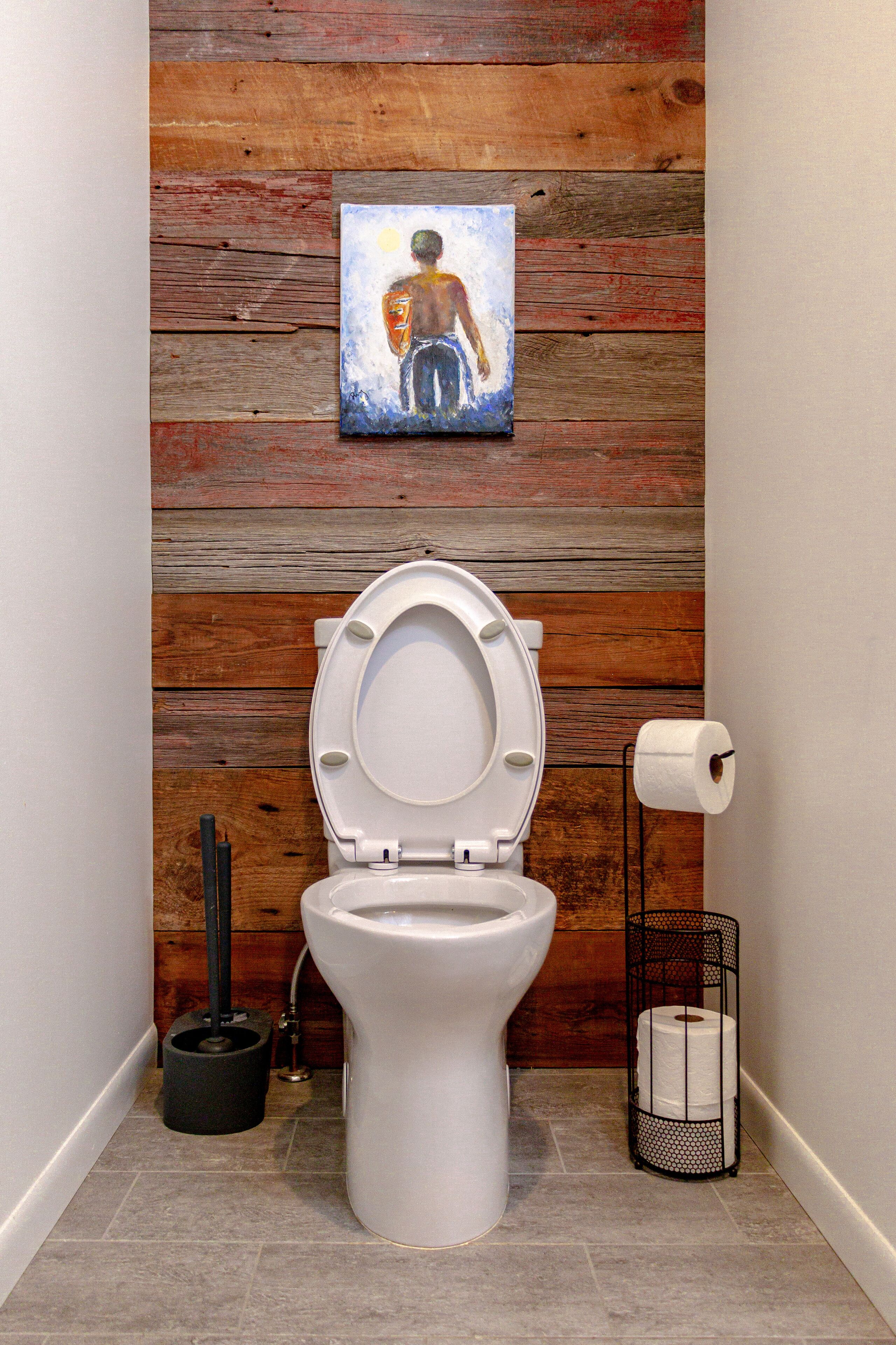 Een badkamer met een houten wand, een wit toilet, een rol toiletpapier en een ontstoppingshaak.