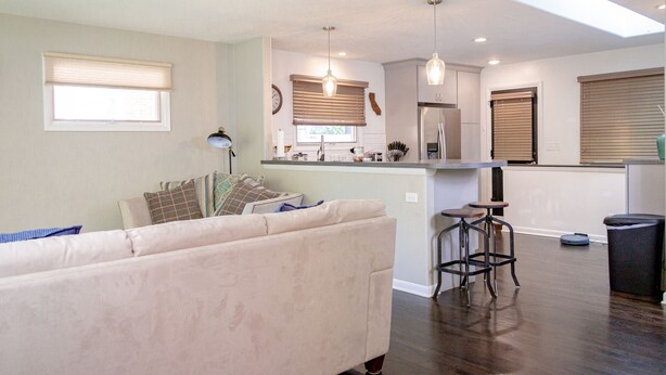 A modern living room with a sofa, a dining area with a bar, and a kitchen in the background.