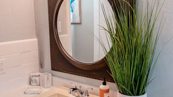 A bathroom with a white sink, a mirror with lights above, a potted plant, and a blue towel on the counter.