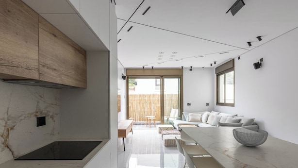 A modern kitchen with white marble countertops, a wooden cabinet, and a dining area with a white sofa and a round woven basket. - Luxury 2BR In Flea Market By Holiday Rentals (Tel Aviv-Yafo)