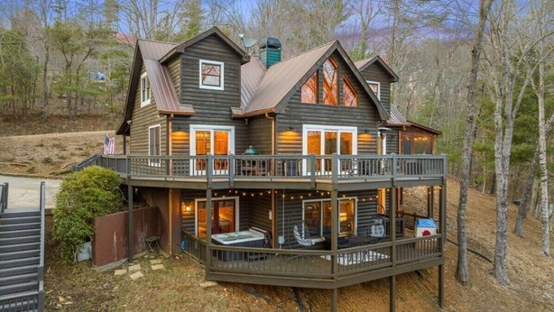 Une cabane en rondins à deux étages, dotée d’un balcon, d’un espace salon extérieur et d’une cheminée.
