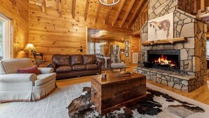 L’intérieur d’un chalet confortable, avec une cheminée en pierre, des murs en bois, des meubles en cuir et un lustre.