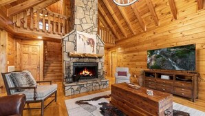 L’intérieur d’une cabane en rondins, avec une cheminée en pierre, des meubles en bois et un grand tableau accroché au mur.