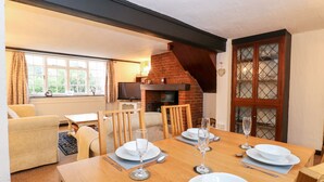 A dining area with a wooden table set for four, a fireplace, and a window with curtains. - Phloxhaven (Norwich)