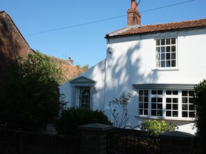 A white building with a brick chimney, a white door, and a window with a white frame. - Phloxhaven (Norwich)