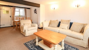 A cozy living room with a sofa, armchairs, a wooden coffee table, and a dining area with a table and chairs. - Phloxhaven (Norwich)