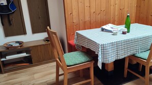 A dining area with a checkered tablecloth, two wooden chairs with green cushions, a green bottle, and a bowl of magazines on a wooden table. - farm💗 for families and vacationers with pets (Eppan)