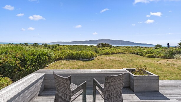 A deck with wicker chairs overlooking a coastal landscape with a distant mountain range. - Island View Beach House - Paraparaumu Beach Home (Paraparaumu)