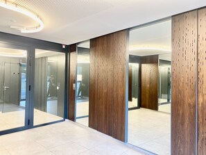 Un espace moderne pour les ascenseurs, doté de portes en verre et de panneaux en bois.