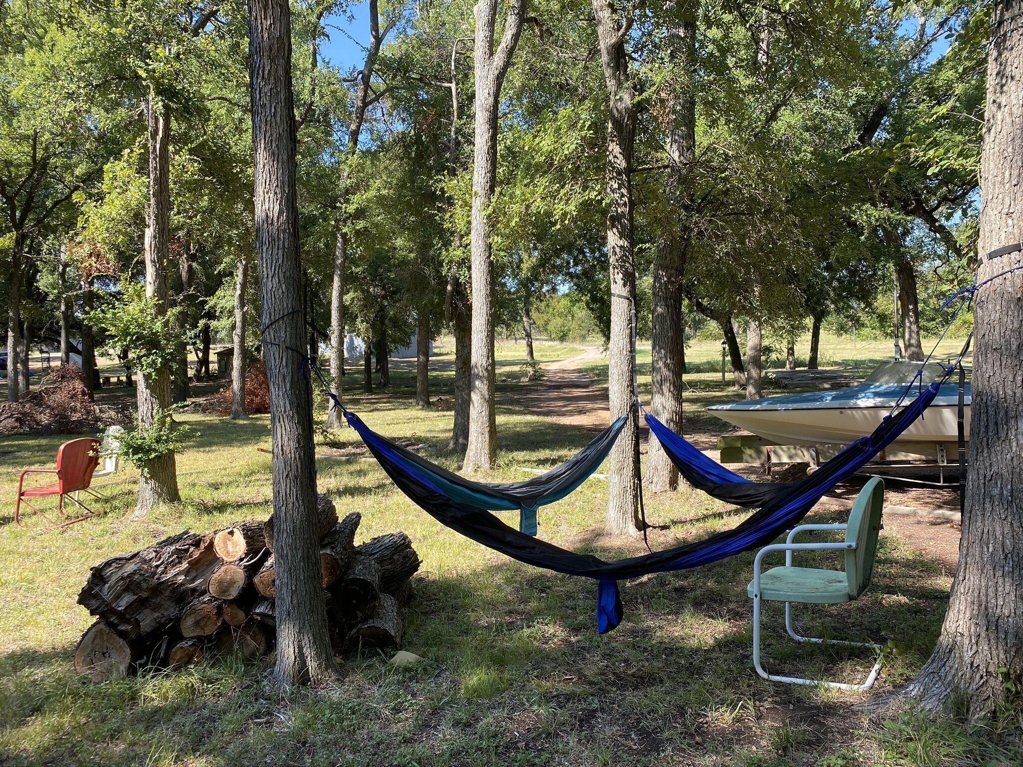 Una hamaca entre árboles en un parque, con una mesa de picnic y un barco al fondo.