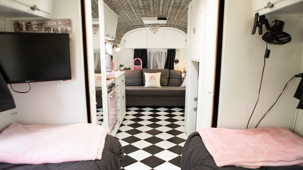 Een compact interieur van een camper met twee bedden, een kitchenette en een leefruimte met een geruit vloertje.