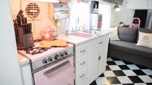 Een keuken met een roze fornuis, witte kasten en een geruite vloer.