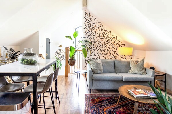 A modern living room with a grey sofa, a coffee table, and a dining area with a marble table and chairs.