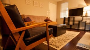 Un salon moderne avec un fauteuil en bois, un canapé, une table basse et un téléviseur.