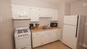 Une petite cuisine avec des meubles blancs, une cuisinière, un four à micro-ondes et un réfrigérateur.