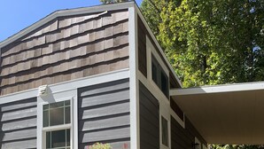 A wooden house with a porch and steps leading to a door. - The Honey Crisp @ Backyard Apple Cottages (FLAT ROCK)