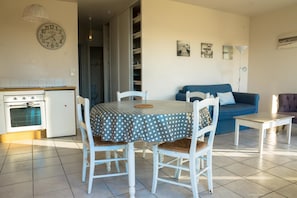 A dining area with a table covered by a polka dot tablecloth, surrounded by white chairs with brown cushions. A blue sofa and a small table are in the background.