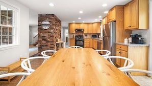 Een moderne keuken met houten kastjes, een accentmuur van baksteen en een centraal eiland met stoelen.