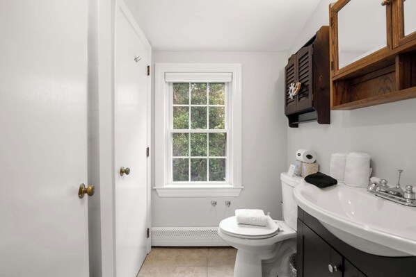 A small, white bathroom with a window, a toilet, and a sink.