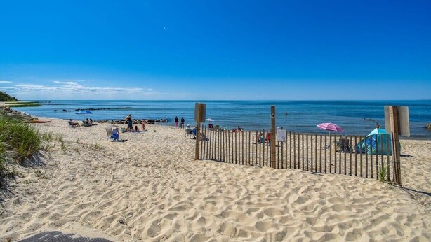 Een zandstrand met een houten omheining, ligbedden en parasols.
