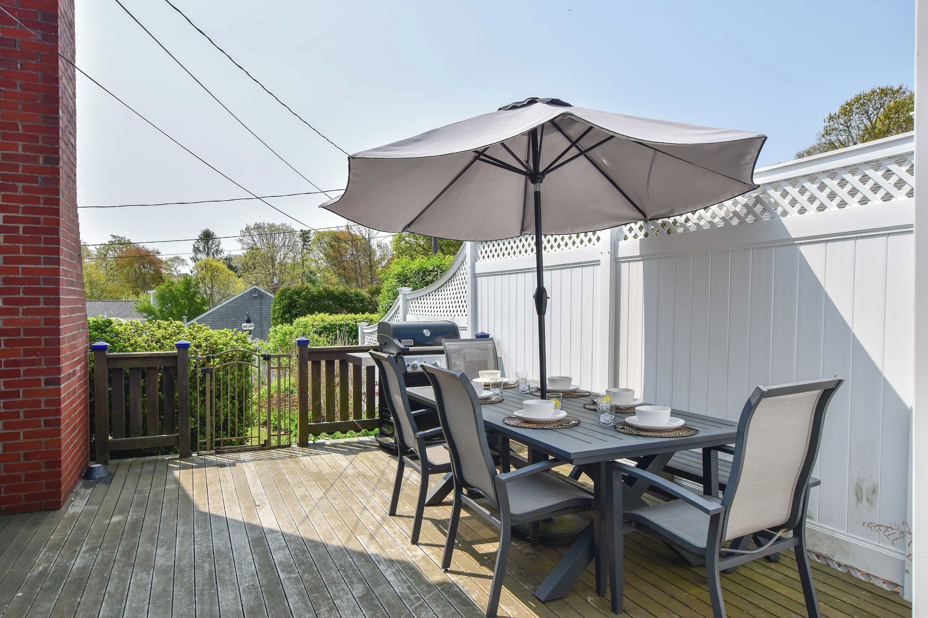 A deck with a table set for dining, outdoor furniture, and a large umbrella providing shade.
