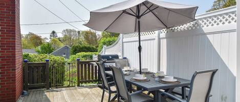 A deck with a table set for dining, outdoor furniture, and a large umbrella providing shade.