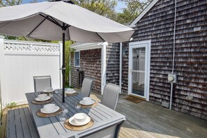 An outdoor dining area with a table set for four, surrounded by chairs, under a large umbrella.