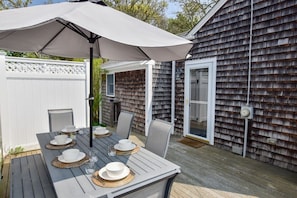 Une terrasse en bois avec une table dressée pour quatre personnes, un parasol et une maison aux murs recouverts de bardeaux.