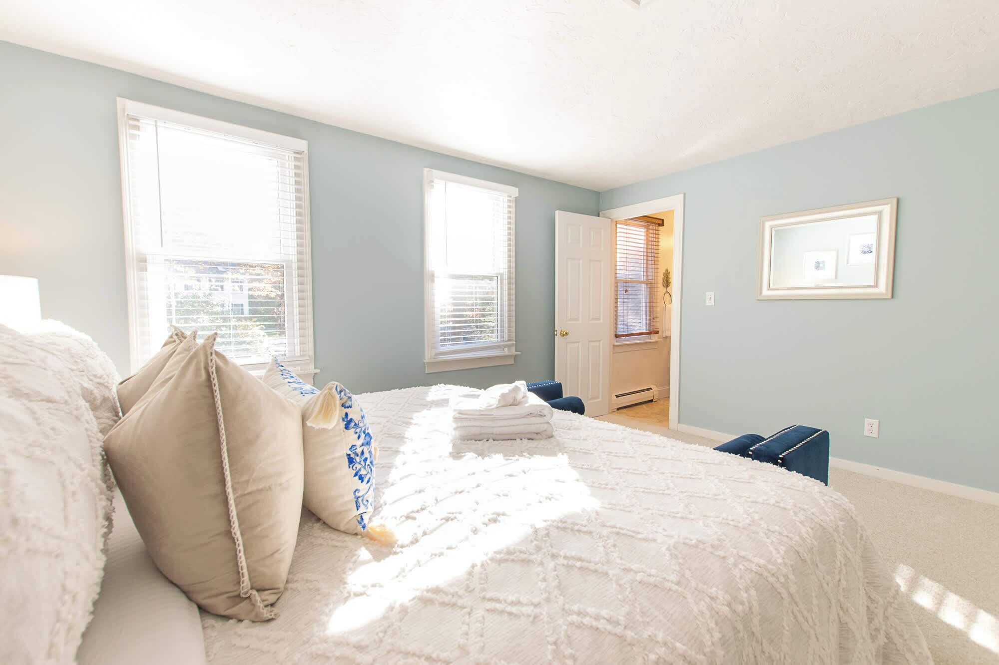 Une chambre à coucher avec un lit, des oreillers, une chaise, une porte et une fenêtre.
