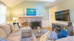 A living room with a fireplace, sofa, TV, and a bookshelf. - Spacious Stone Fire Pit Game Room! (Marstons Mills)