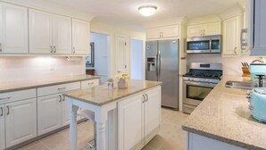 A modern kitchen with white cabinets, granite countertops, stainless steel appliances, and a central island. - Spacious Stone Fire Pit Game Room! (Marstons Mills)