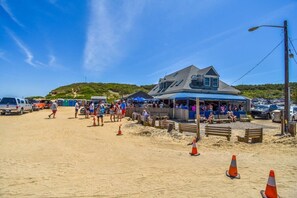 Un edificio frente a la playa, con techo azul, rodeado de gente y vehículos estacionados.