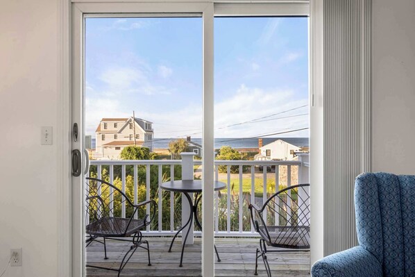 A balcony with a view of houses and the ocean, a metal chair, and a small table. - Stunning Home with Water Views! (Sandwich)