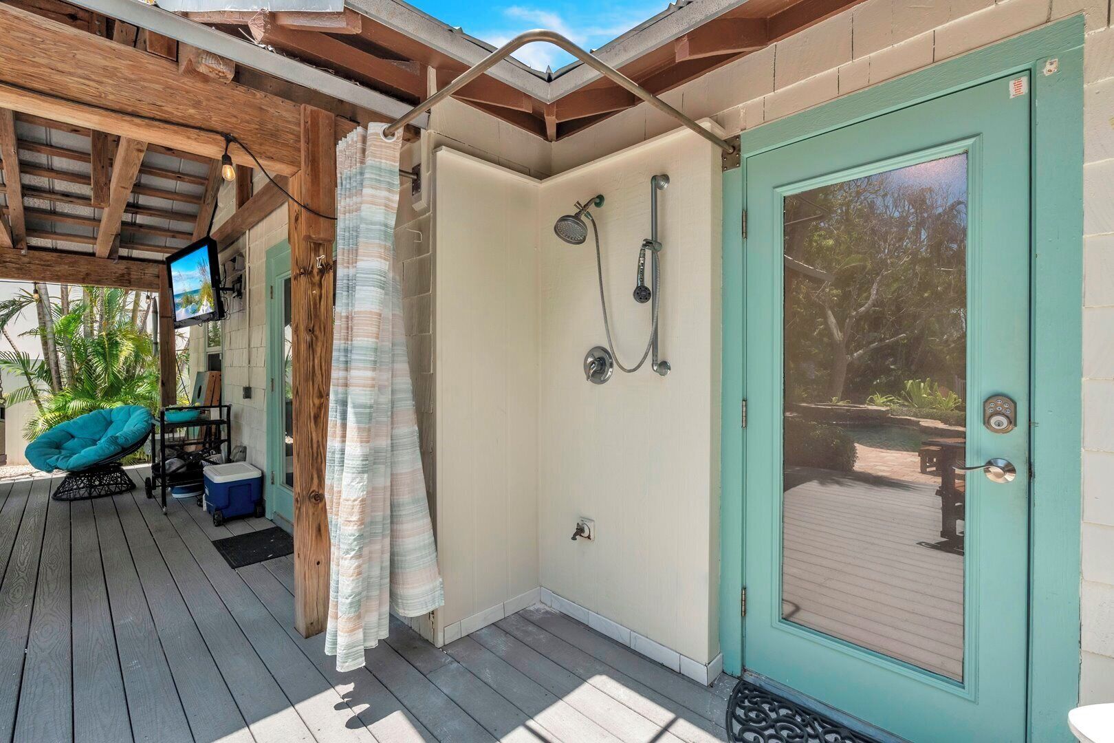 A covered outdoor shower area with a wooden ceiling, a teal door, and a view of a pool.