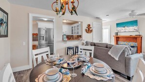 A dining area with a round table set for four, a modern kitchen in the background, and a living room with a gray sofa. - Shady Mango by Duncan Real Estate (Anna Maria)