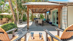 A wooden deck with outdoor furniture, a grill, and a TV screen. - Shady Mango by Duncan Real Estate (Anna Maria)