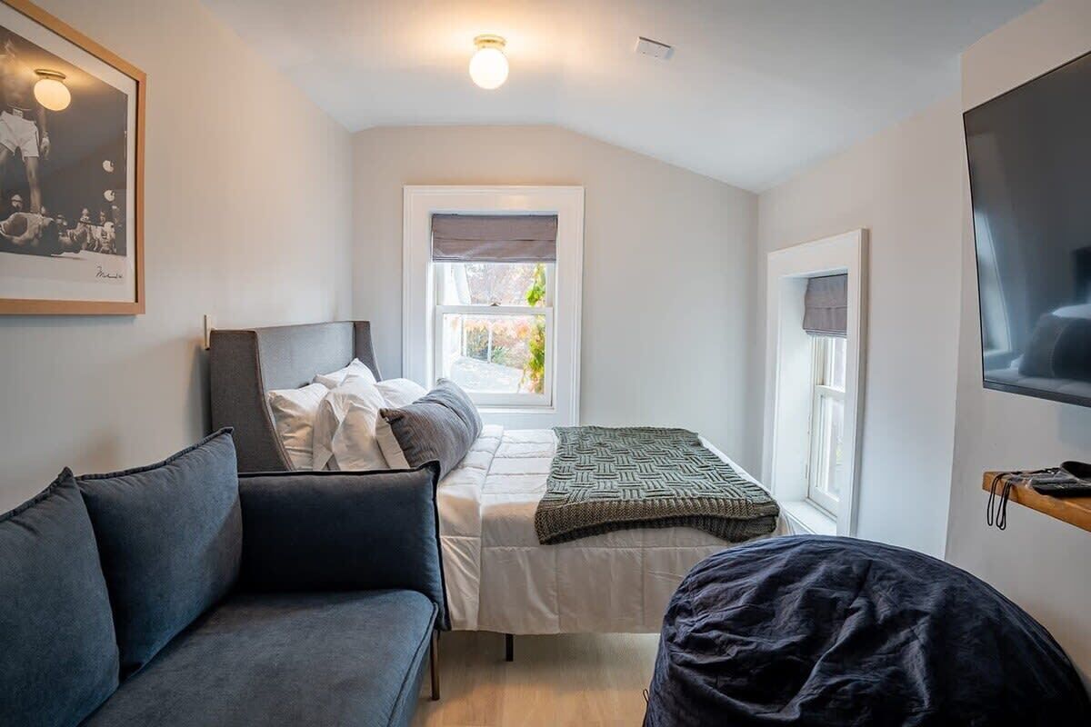 A compact bedroom with a bed, a sofa, a TV, and a window with a view of greenery.