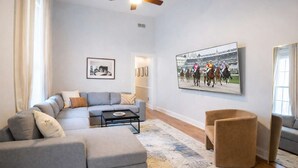 Una sala de estar moderna con un sofá seccional gris, una mesita redonda y un cuadro grande enmarcado de una carrera de caballos.