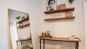 Una habitación con un espejo grande, estantes de madera con vasos, una mesita con una vela y dos bancos acolchados.