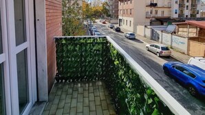 Un balcón con suelo de baldosas, vista a una calle con coches y edificios al fondo.