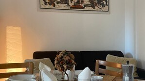Una mesa de comedor preparada con platos, tazas y una cafetera, con un cuadro encima y una lámpara a la izquierda.