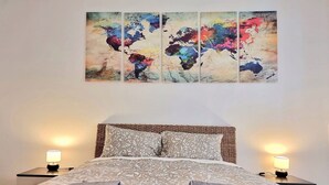 Una cama bien hecha con colcha estampada y almohadas, dos lámparas de noche, y una obra de arte con un mapa del mundo sobre la cama.