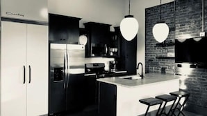 A modern kitchen with stainless steel appliances, a central island with bar stools, and pendant lighting. - Historic Penthouse Style Loft in OTR, Parking Included (Cincinnati)