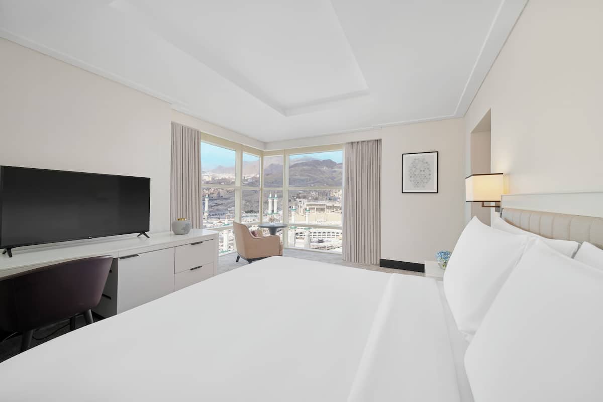 Une chambre d’hôtel avec un grand lit, un bureau doté d’un téléviseur à écran plat, une chaise, une fenêtre donnant sur la ville et une lampe.