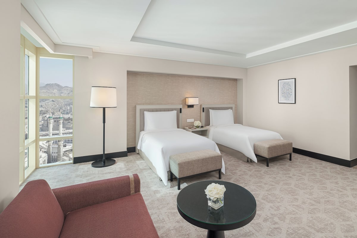 Une chambre d’hôtel avec deux lits, un canapé, une table ronde, une lampe et une vue sur le paysage urbain.