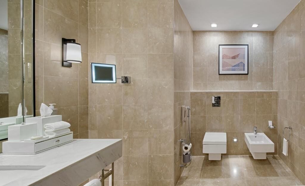 A modern bathroom with a large mirror, a vanity with toiletries, a shower area, and a sink.