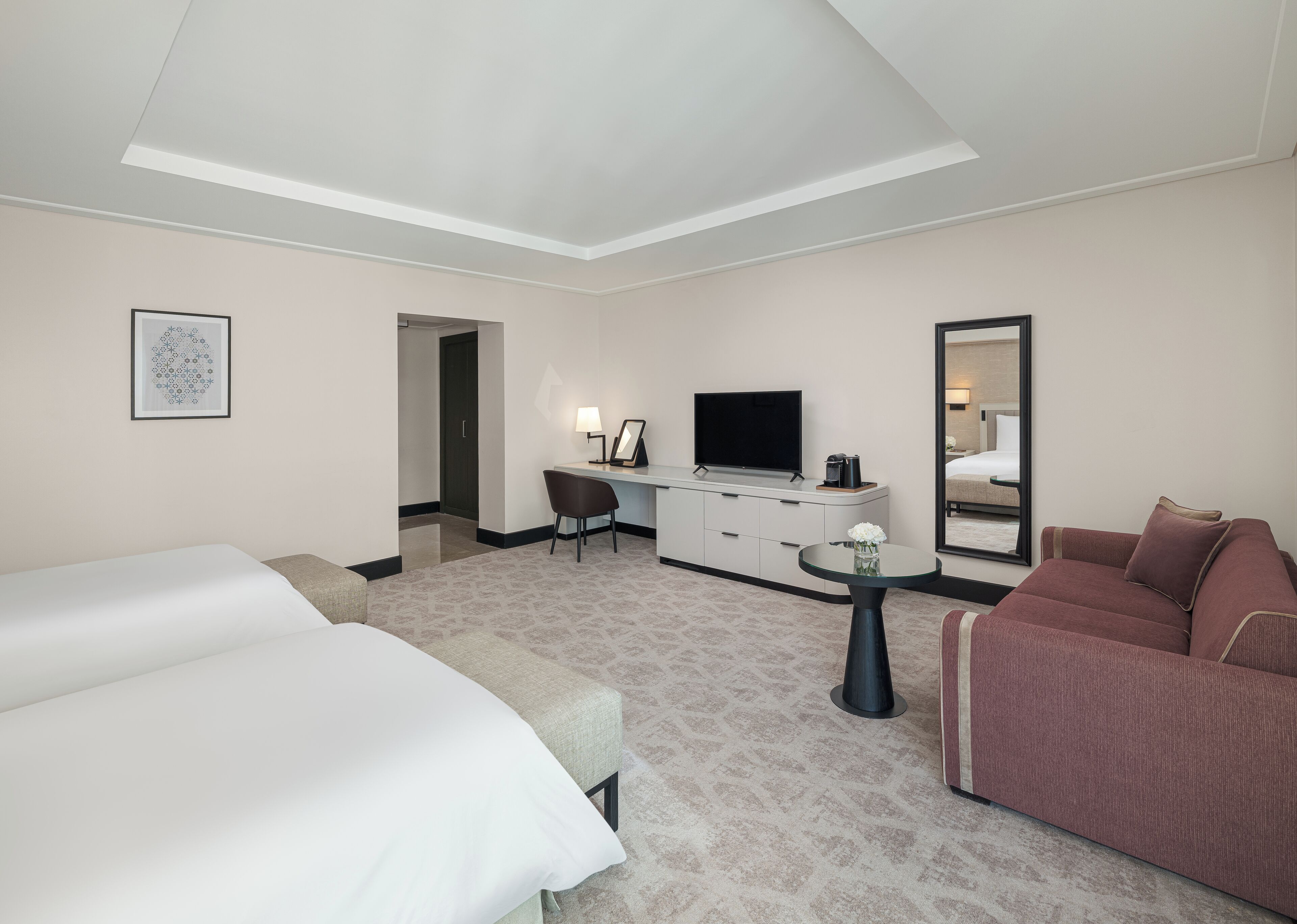 Una habitación de hotel con cama, escritorio con televisor, sofá y espejo.