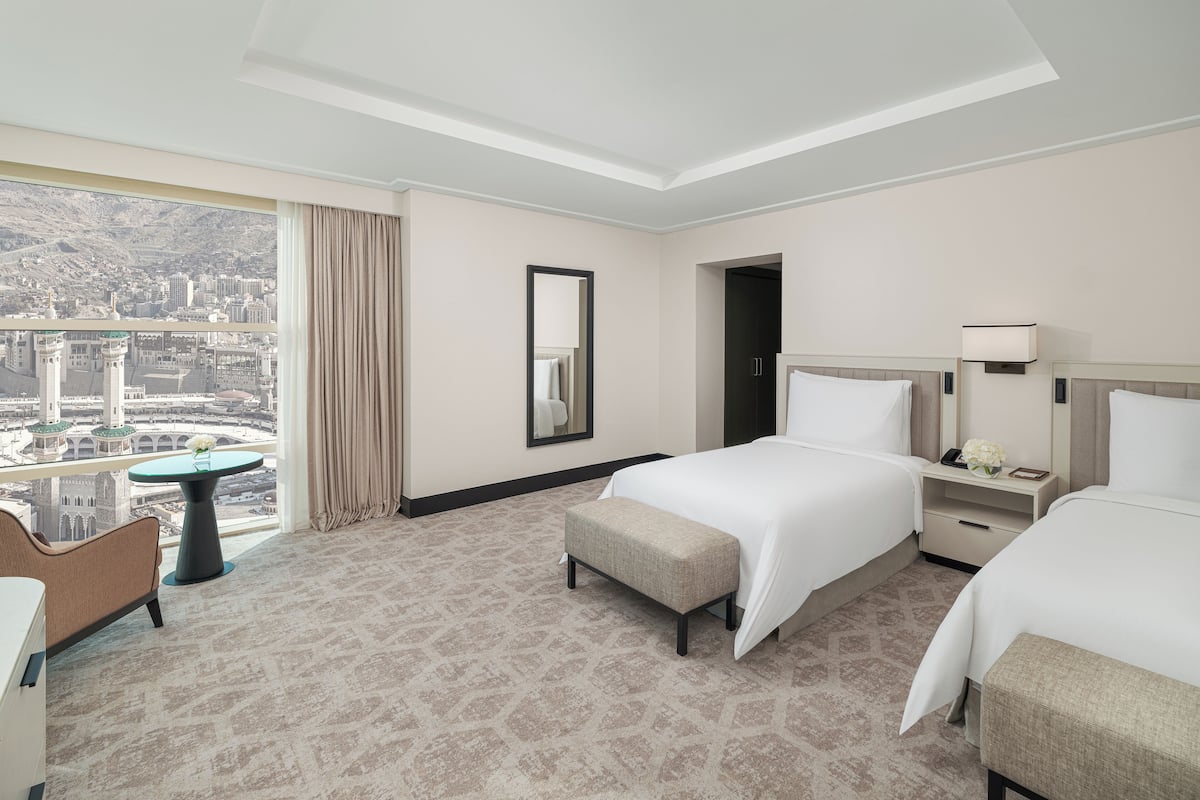 Une chambre d’hôtel avec deux lits, un bureau, une chaise, une petite table et une grande fenêtre donnant sur la ville.