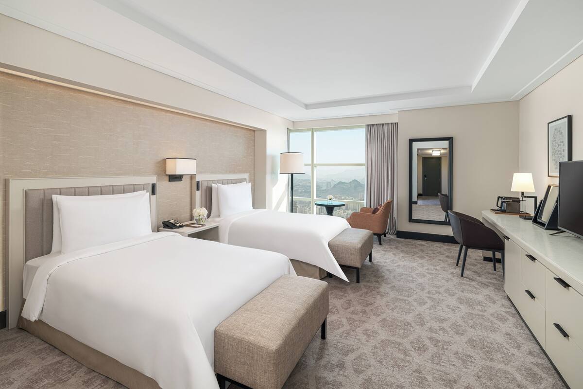 Une chambre d’hôtel avec deux lits, un bureau, une chaise, une télévision et une vue sur la ville.